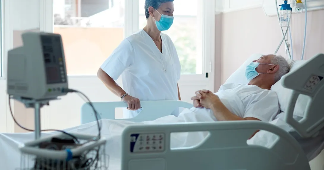 Healthcare provider standing next to a patient lying down in a hospital bed Healthcare provider standing next to a patient in a hospital bed