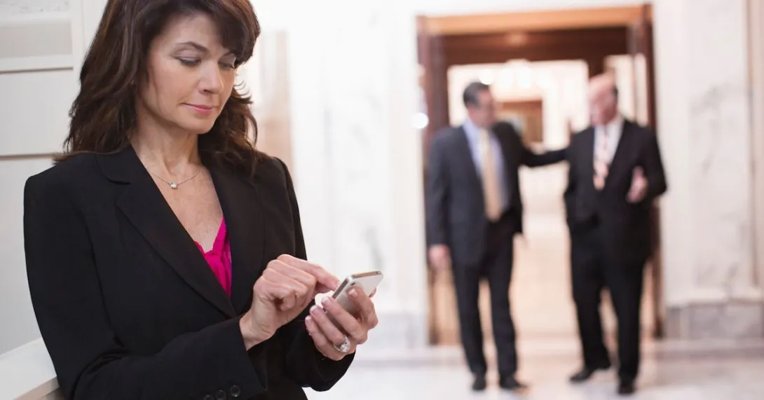 Person standing in a corridor with two other people behind them walking Person standing in a corridor with two other people behind them walking