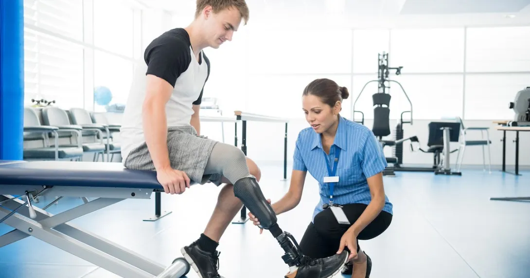 Person with a prosthetic leg undergoing physical therapy with a physical therapist beside them Person with a prosthetic leg undergoing physical therapy with a physical therapist beside them