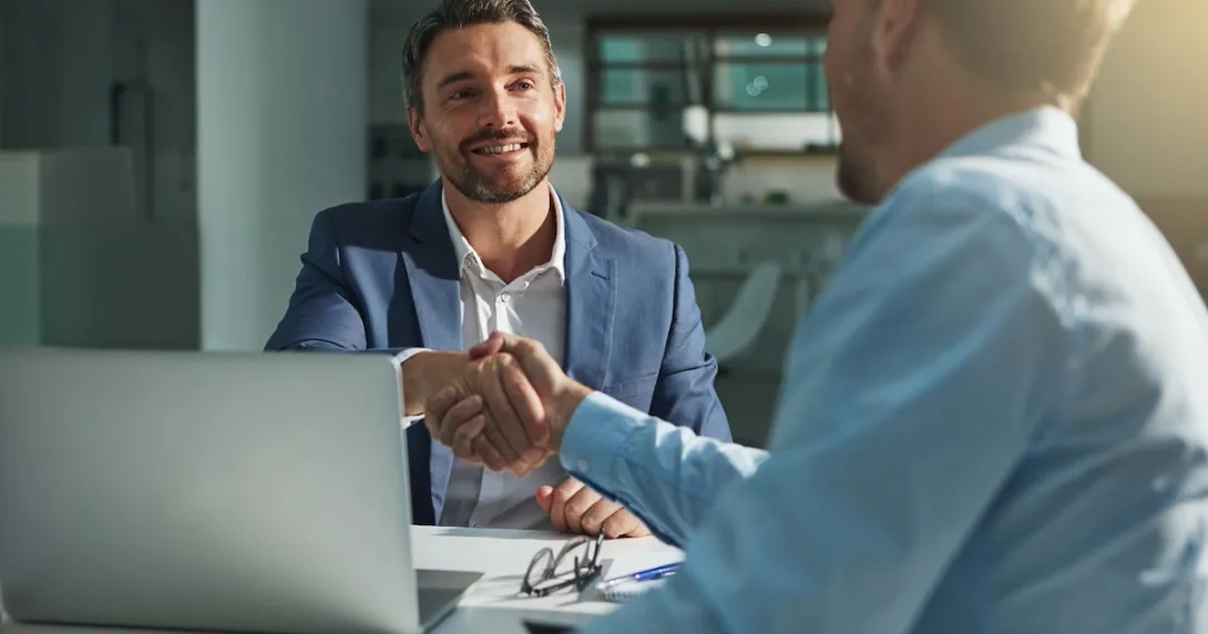 Two people sitting across from each other at a table and shaking hands Two people sitting across from each other at a table and shaking hands