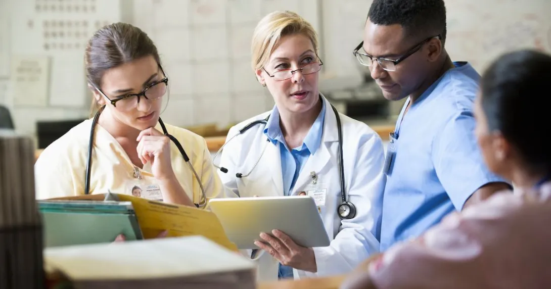 Three healthcare providers sitting together looking at a tablet together Three healthcare providers sitting together looking at a tablet together