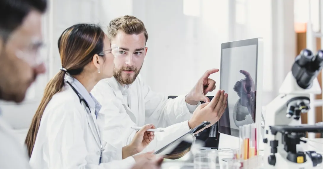 Two people standing in a laboratory looking at a computer Two people standing in a laboratory looking at a computer