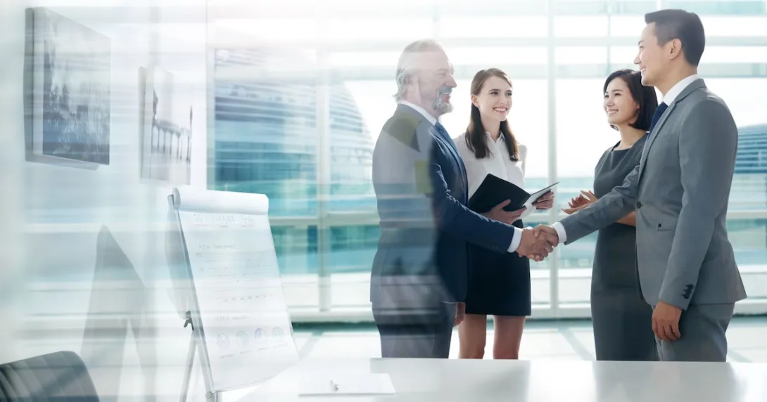 Two people shaking hands with two more people watching Two people shaking hands with two more people watching