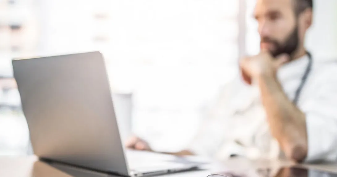 Healthcare provider sitting at a desk while wearing a stethoscope around their neck and looking at a computer Healthcare provider sitting at a desk while wearing a stethoscope around their neck and looking at a computer