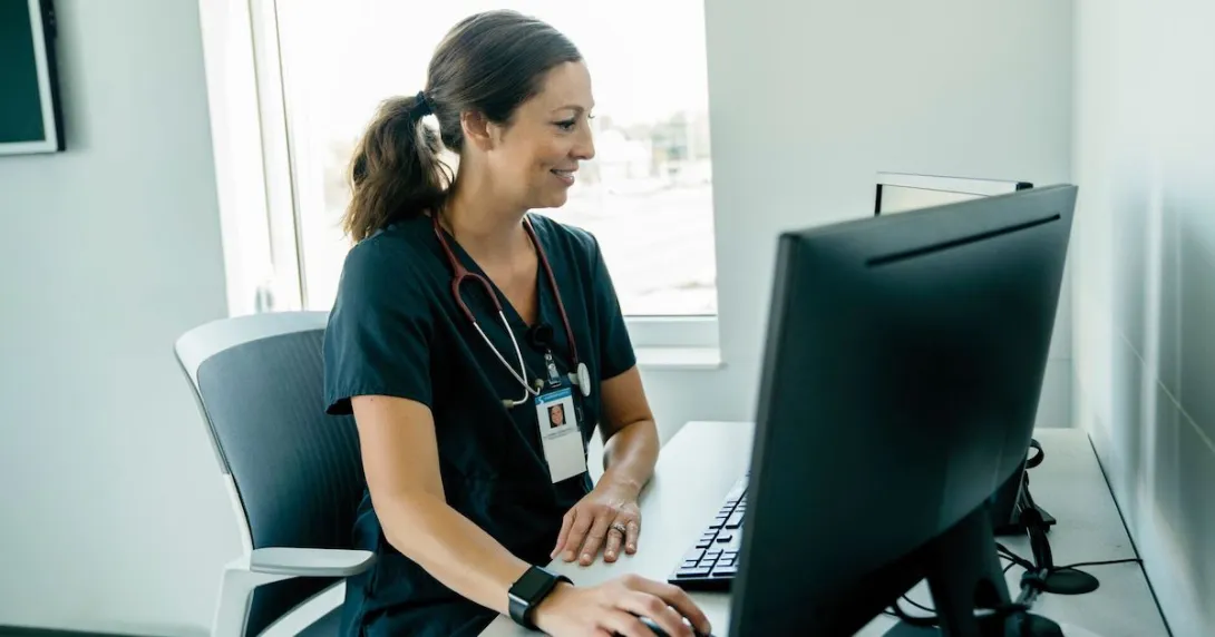 Person wearing nursing scrubs sitting at desktop Person wearing nursing scrubs sitting at desktop