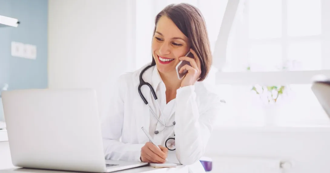 A doctor on the phone while checking a patient's record on a laptop computer A doctor on the phone while checking a patient's record on a laptop computer
