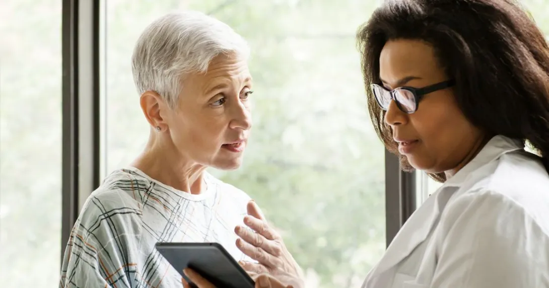 An elderly patient talking to a doctor who is holding a tablet An elderly patient talking to a doctor who is holding a tablet
