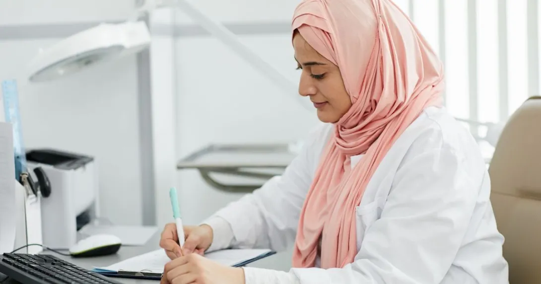 A nurse wearing a hijab filing a patient's form at a desk A nurse wearing a hijab filing a patient's form at a desk