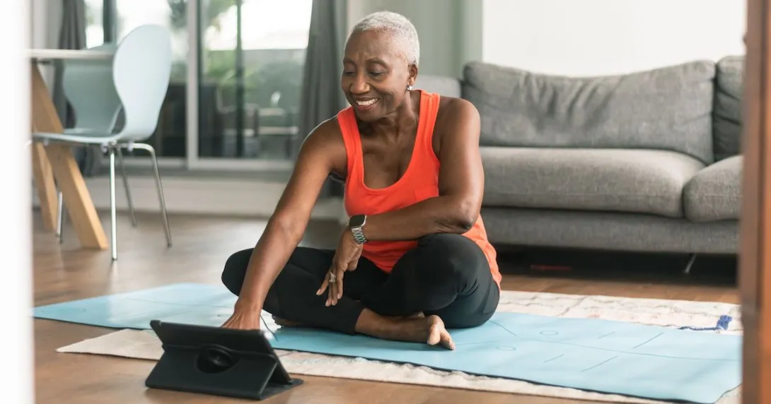 A person sitting on a yoga mat wearing workout clothes looking at tablet A person sitting on a yoga mat wearing workout clothes looking at tablet