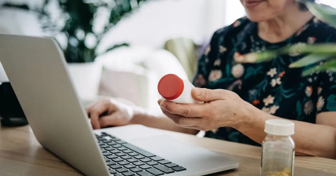 A woman holding a pill bottle using a laptop A woman holding a pill bottle using a laptop