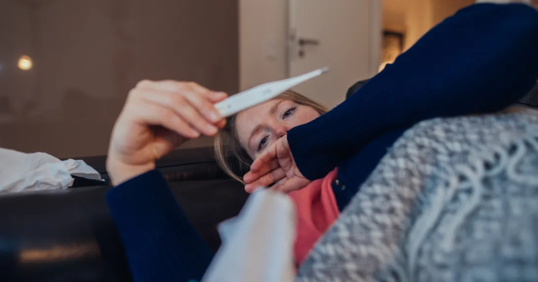 A sick woman looking at a thermometer