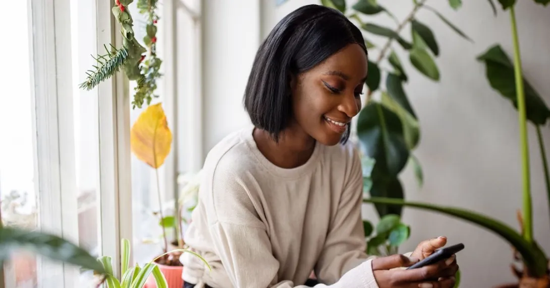 A young woman sitting near a window using a smartphone A young woman sitting near a window using a smartphone