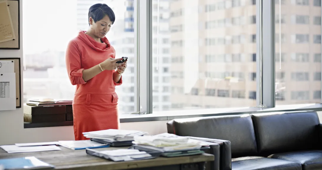 A woman standing at her desk looking at a smartphoneP A person standing at desk looking at a smartphone