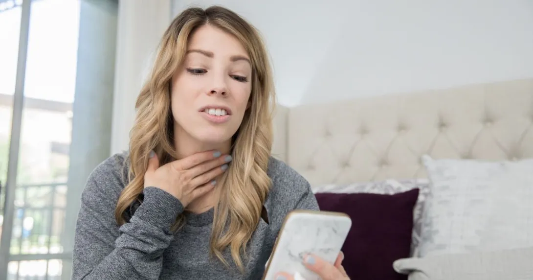A woman rubbing her sore throat holding a smartphone. A woman rubbing her sore throat holding a smartphone.