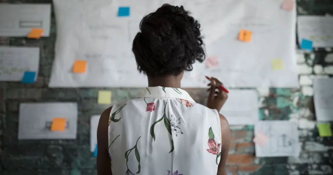 A woman standing with her back to the camera before a wall covered in planning documents and post-it notes A woman standing with her back to the camera before a wall covered in planning documents and post-it notes
