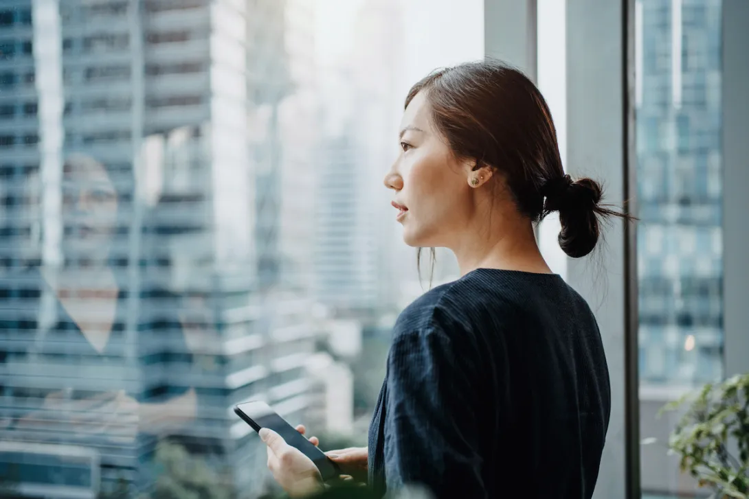 A young woman using a smartphone and looking out a window. A young woman using a smartphone and looking out a window.
